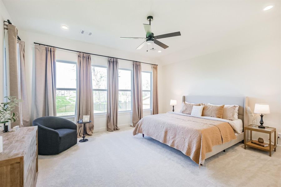 Spacious and cozy primary bedroom with carpet and wall of windows to the beautiful green space.