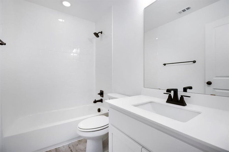 Bathroom featuring a white subway tile tub surround, white vanity with integrated sink, matte black fixtures, and a large wall-mounted mirror Bathroom featuring a white subway tile tub surround, white vanity with integrated sink, matte black fixtures, and a large wall-mounted mirror