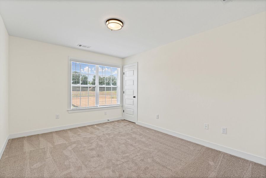Carpeted room featuring a double window with blinds, a six-panel interior door, and a flush-mount ceiling light fixture Carpeted room featuring a double window with blinds, a six-panel interior door, and a flush-mount ceiling light fixture