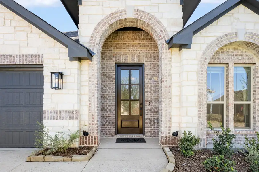Home entrance with brick arched entryway, dark wood front door, stone exterior, and attached garage