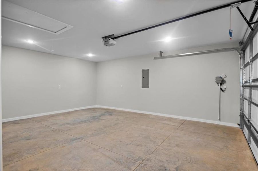 Garage featuring electric panel, a garage door opener, baseboards, and recessed lighting