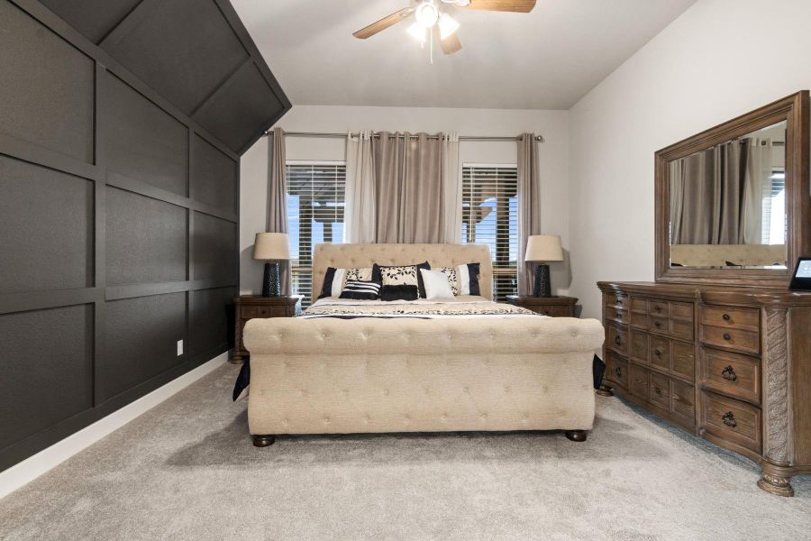 This spacious bedroom features a lot natural light that flows in through large windows with stylish curtains, and a ceiling fan adding comfort. Perfect for relaxation and comfort.