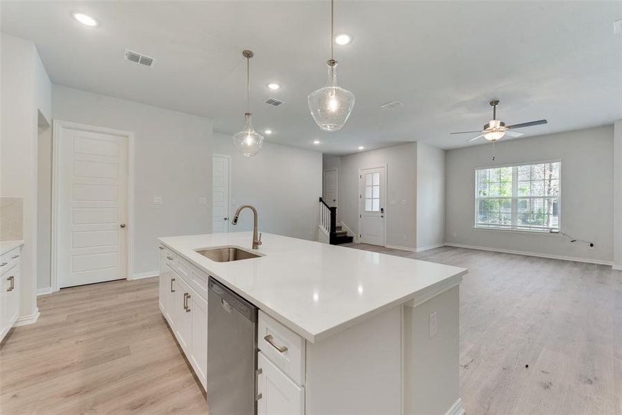 Kitchen featuring stainless steel dishwasher, pendant lighting, sink, a center island with sink, and light hardwood / wood-style floors