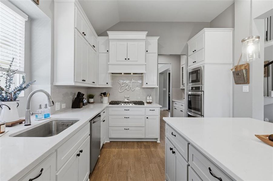 Spacious kitchen featuring white cabinetry, light countertops, wood-finish flooring, a stainless steel sink, and built-in stainless steel appliances