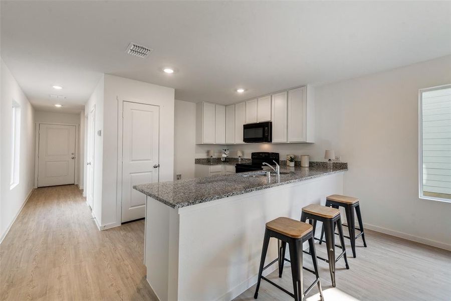 Kitchen with kitchen peninsula, light hardwood / wood-style flooring, black appliances, a breakfast bar area, and dark stone counters