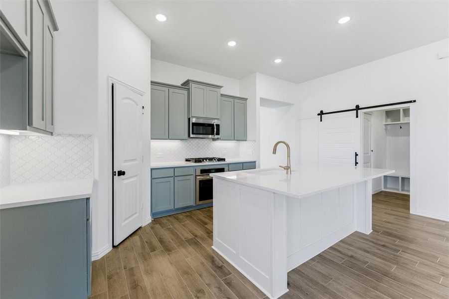 Kitchen featuring a barn door, wood finish floors, light stone countertops, stainless steel appliances, and recessed lighting