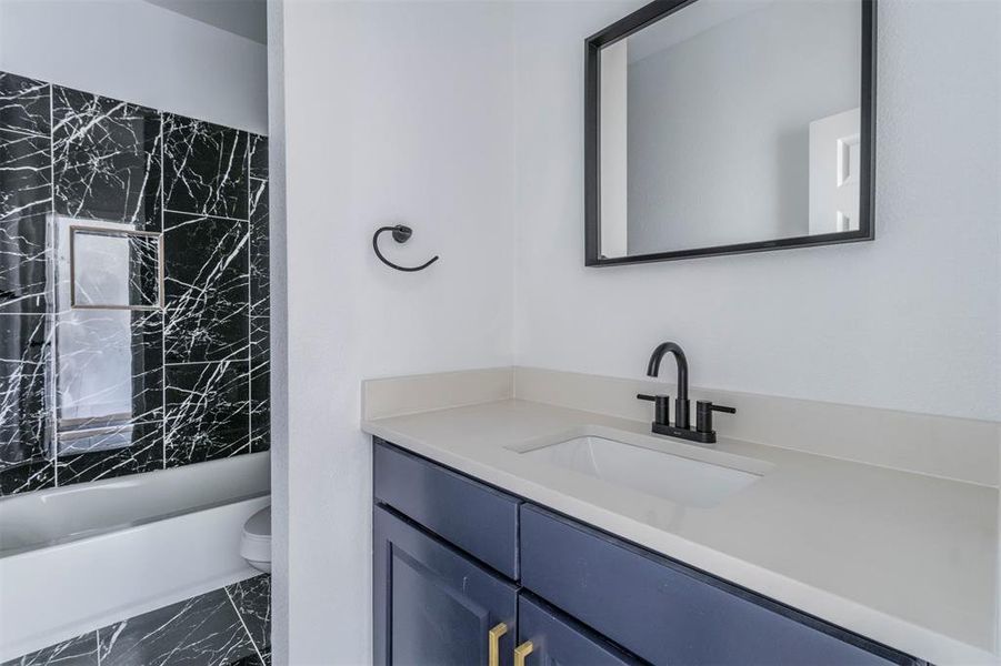 Full bathroom with marble finish flooring, toilet, vanity, and bathtub / shower combination Full bathroom with marble finish flooring, toilet, vanity, and bathtub / shower combination