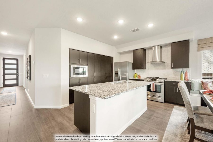 Kitchen with large granite island, dark cabinets, stainless steel appliances, and hardwood floors open to entryway Kitchen with large granite island, dark cabinets, stainless steel appliances, and hardwood floors open to entryway