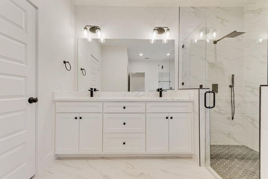 Full bathroom featuring light marble finish flooring, double vanity, and a marble finish shower Full bathroom featuring light marble finish flooring, double vanity, and a marble finish shower