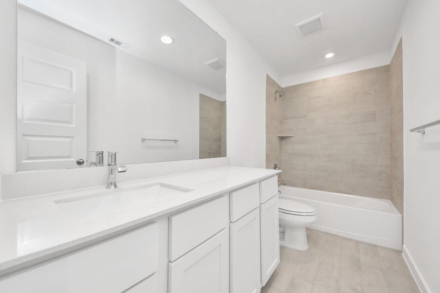 Secondary bath features tile flooring, bath/shower combo with tile surround, light stained wood cabinets, beautiful light countertop.