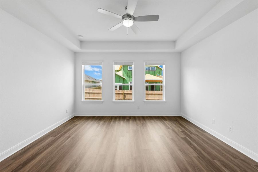 A well-lit bedroom with three bright windows and sleek wood flooring offers a tranquil retreat.