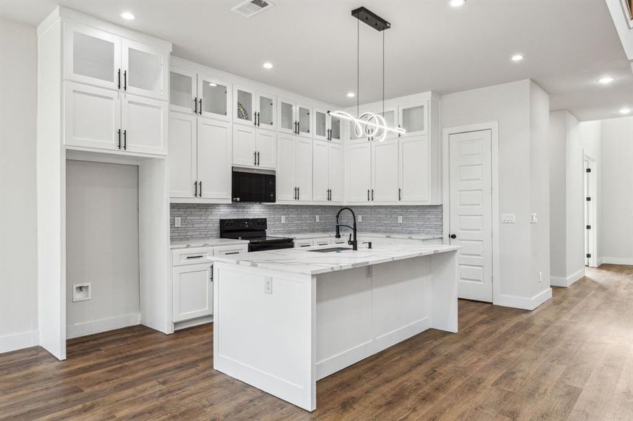 Kitchen featuring black appliances, light stone countertops, an island with sink, and white cabinetry