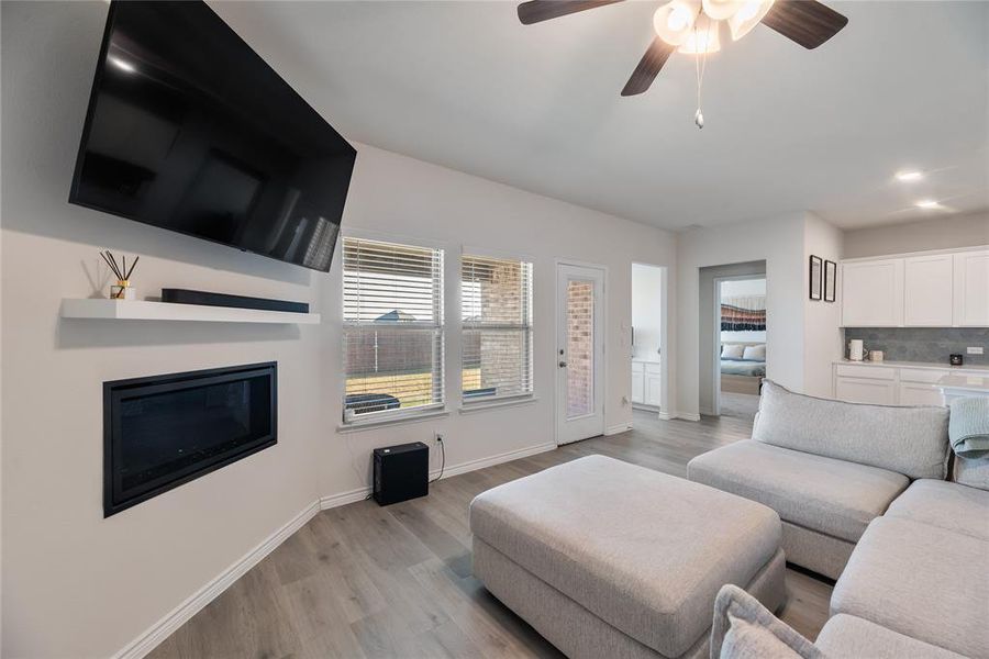 Living room featuring light wood-style flooring, ceiling fan, a glass covered fireplace, and recessed lighting