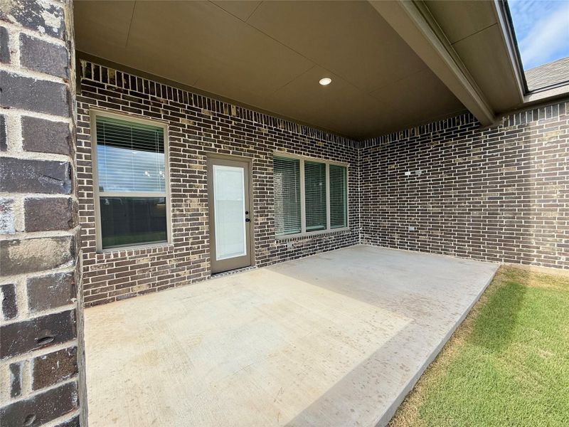 Covered patio area featuring a concrete slab, dark brick exterior, recessed lighting, and a glass-paneled door