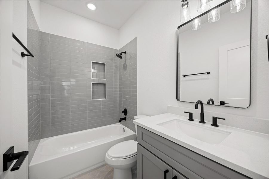 This secondary bathroom boasts tile flooring, a bath/shower combo with a stylish tile surround, stained wood cabinetry, elegant light countertops, a mirror, and sleek dark fixtures complemented by modern finishes. This secondary bathroom boasts tile flooring, a bath/shower combo with a stylish tile surround, stained wood cabinetry, elegant light countertops, a mirror, and sleek dark fixtures complemented by modern finishes.