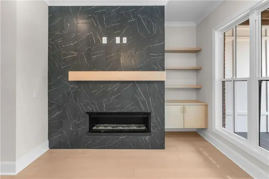 Floor-to-ceiling marbled-pattern tile fireplace surround with a wood mantel, built-in shelving, a built-in cabinet, and wood-finish flooring