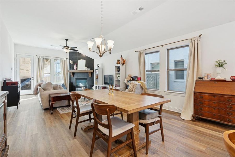 Dining room featuring a chandelier, light wood-style flooring, lofted ceiling, a ceiling fan, and a tile fireplace Dining room featuring a chandelier, light wood-style flooring, lofted ceiling, a ceiling fan, and a tile fireplace
