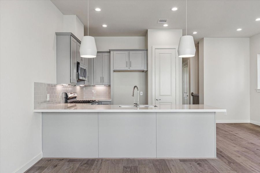 The heart of the home features a massive quartz island and designer pendant lighting, offering an expansive, airy space perfect for gathering and culinary creativity.