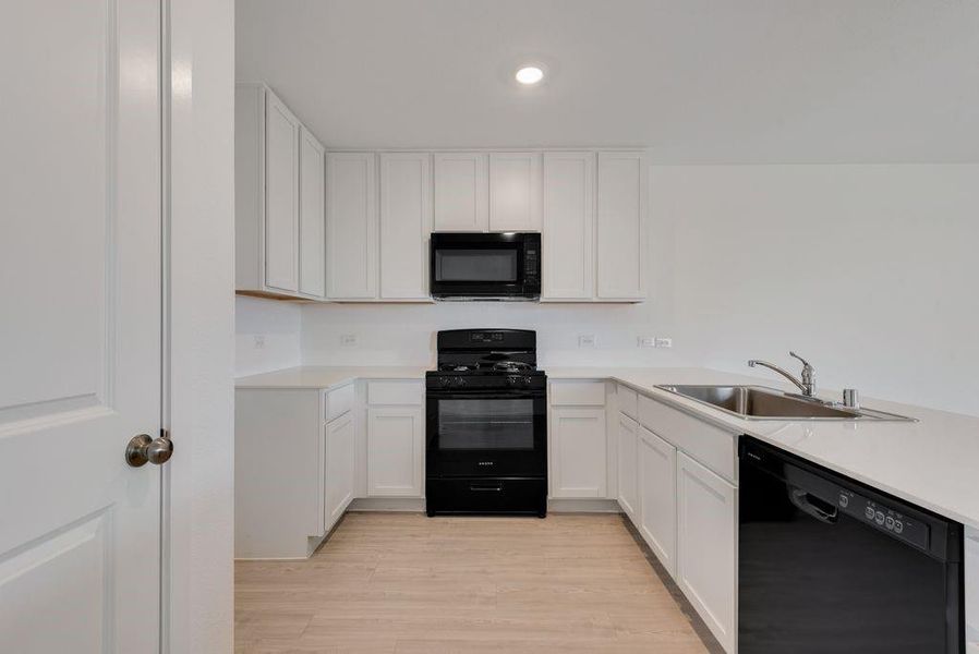 Kitchen with black appliances, light countertops, white cabinetry, and recessed lighting