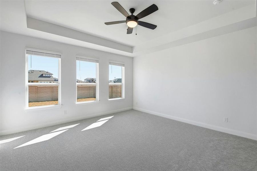 Carpeted interior space featuring a tray ceiling with a ceiling fan