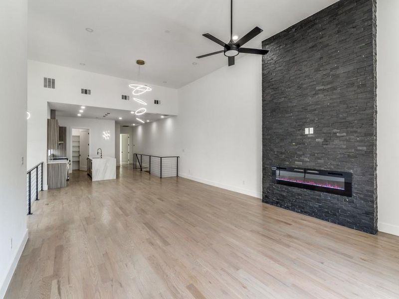 Unfurnished living room with a high ceiling, light wood-style flooring, a ceiling fan, and a stone fireplace