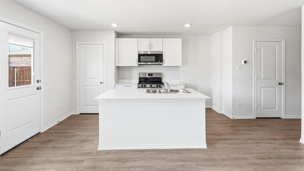 Kitchen with stainless steel appliances, a kitchen island with sink, white cabinetry, light wood finished floors, and recessed lighting