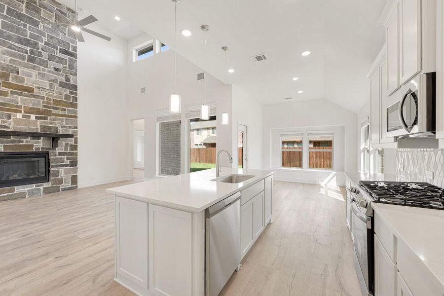Open-concept kitchen with white cabinets, large island, and stone fireplace visible in adjoining living area with vaulted ceiling