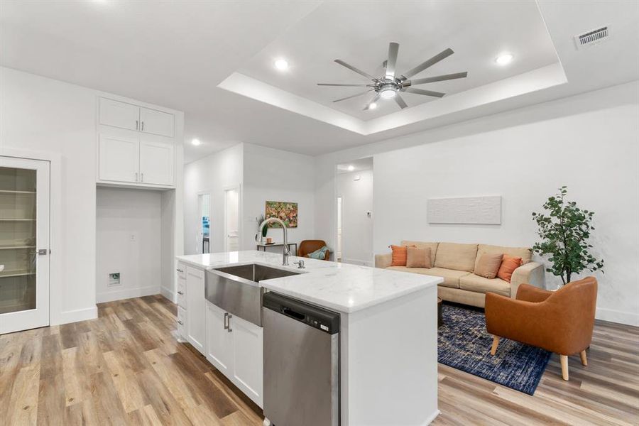 Kitchen with a raised ceiling, a center island with sink, sink, stainless steel dishwasher, and white cabinetry