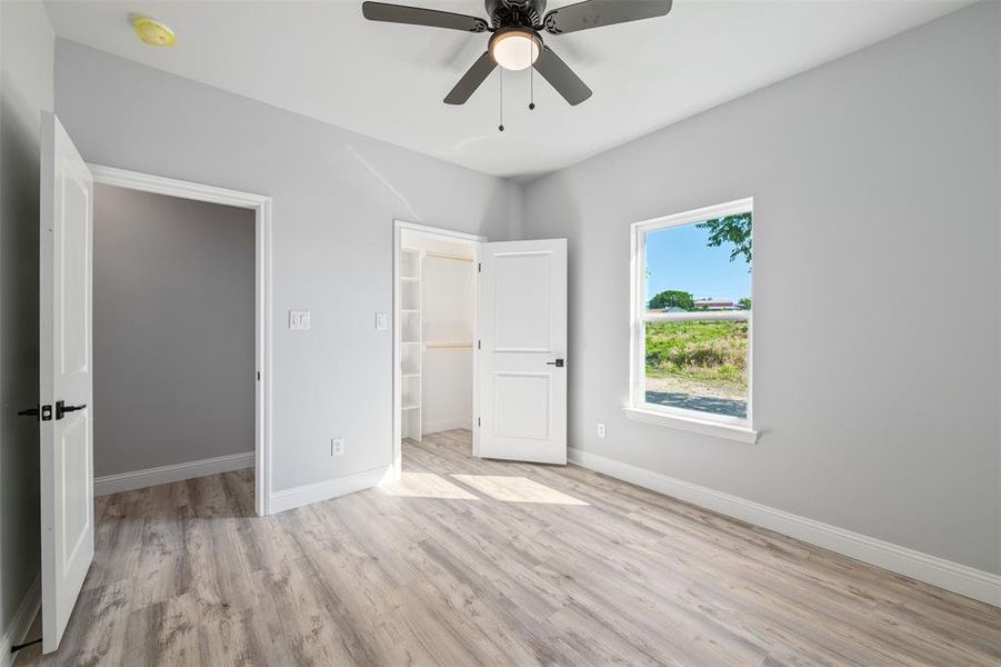 Unfurnished bedroom with a spacious closet, wood finished floors, a closet, and ceiling fan Unfurnished bedroom with a spacious closet, wood finished floors, a closet, and ceiling fan