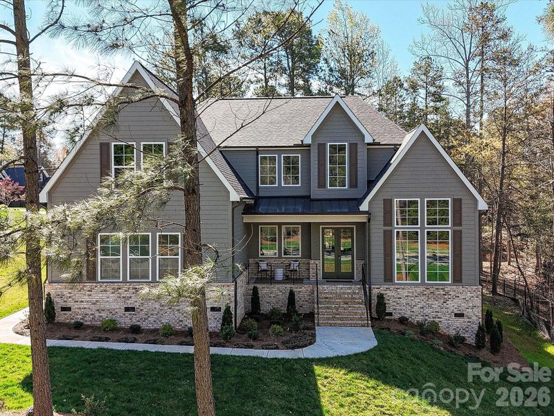 Stunning craftsman-style home with charming covered front porch, stone accents, and nestled on a private, wooded lot offering both curb appeal and peaceful surroundings.
