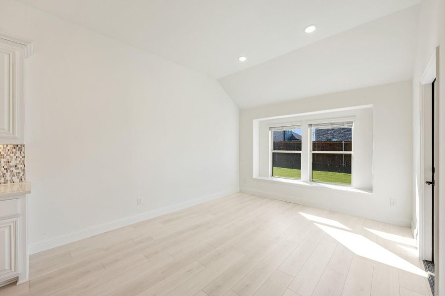 Empty living area with vaulted ceiling, light wood floors, and large window overlooking backyard Empty living area with vaulted ceiling, light wood floors, and large window overlooking backyard
