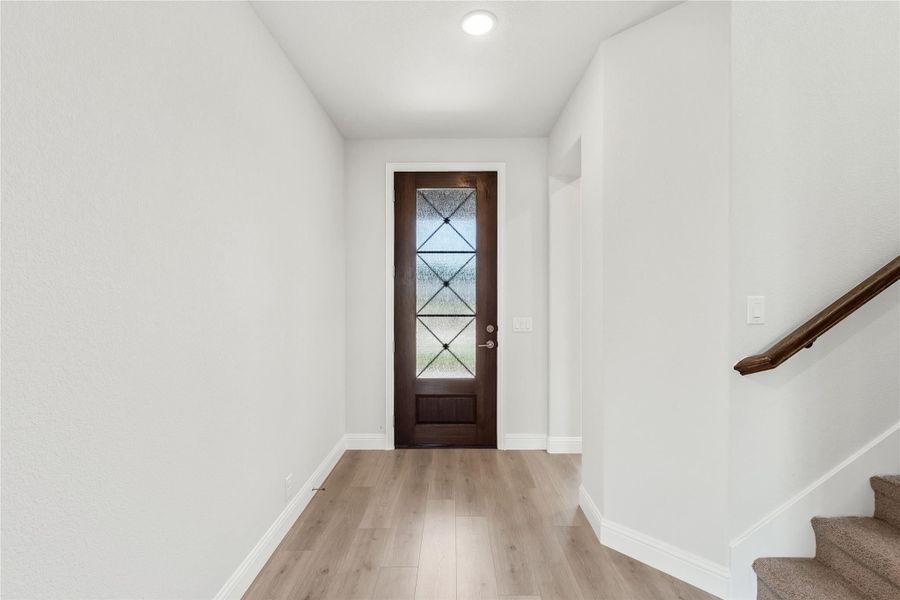Entryway with dark wood front door, decorative glass panel, light wood floors, and staircase with wood railing Entryway with dark wood front door, decorative glass panel, light wood floors, and staircase with wood railing