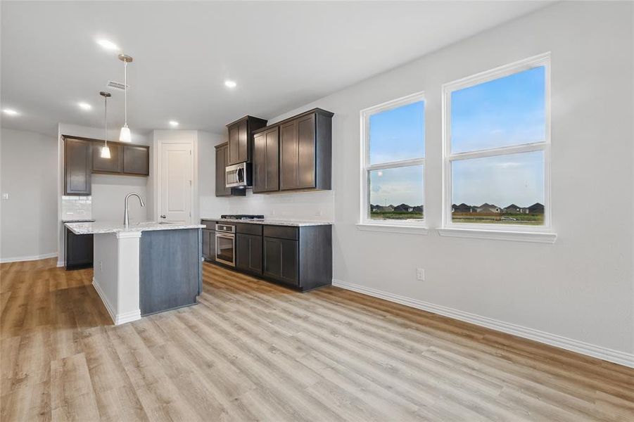 Kitchen with appliances with stainless steel finishes, light wood-type flooring, recessed lighting, pendant lighting, and dark brown cabinets Kitchen with appliances with stainless steel finishes, light wood-type flooring, recessed lighting, pendant lighting, and dark brown cabinets