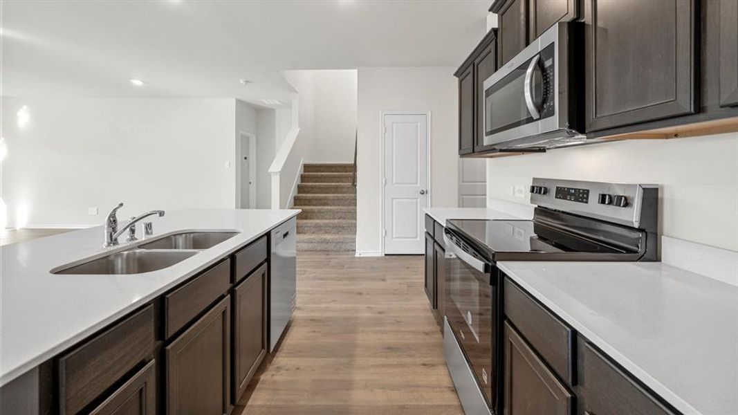 Kitchen featuring stainless steel appliances, light wood-type flooring, dark wood finish cabinets, light stone counters, and recessed lighting