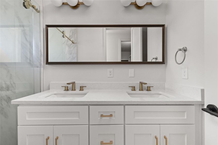 Full bath featuring double vanity and a marble finish shower