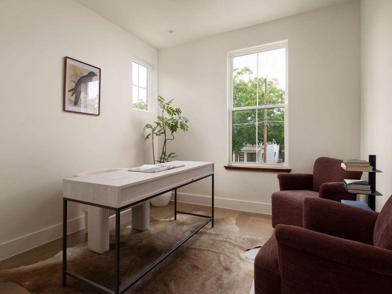 A quiet retreat, perfect for focused work or relaxed reading, features tall windows and rich hardwood underfoot.