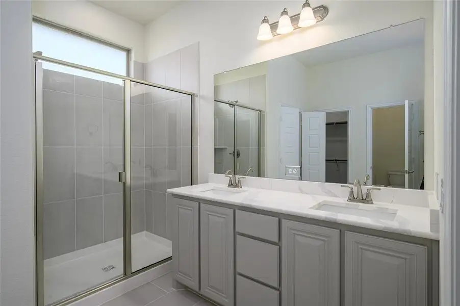 Bathroom featuring walk in shower, tile patterned flooring, toilet, and double sink vanity