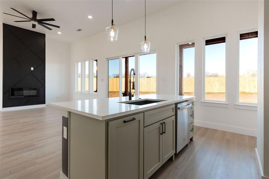 Kitchen with a center island with sink, open floor plan, light wood-style floors, pendant lighting, and dishwasher