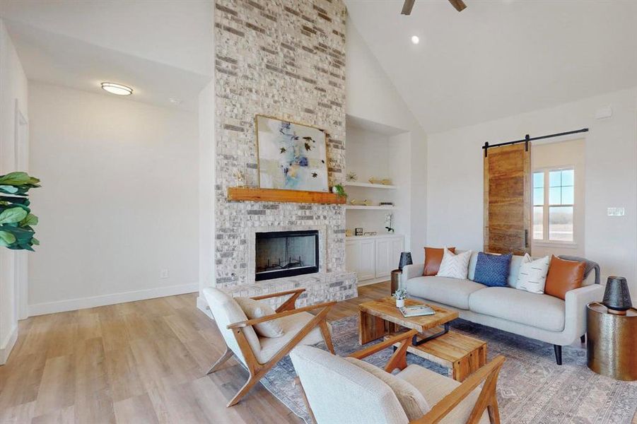 Living room featuring light hardwood / wood-style flooring, ceiling fan, high vaulted ceiling, a brick fireplace, and a barn door