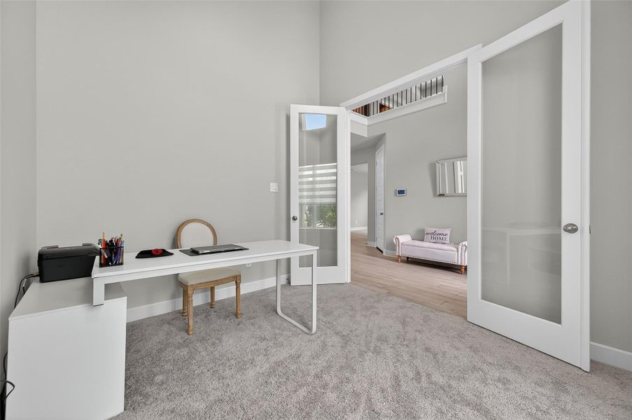 Stylish French doors open to a flexible workspace with plush carpeting and soaring ceilings. The layout flows seamlessly into the hallway, offering privacy without feeling closed off.