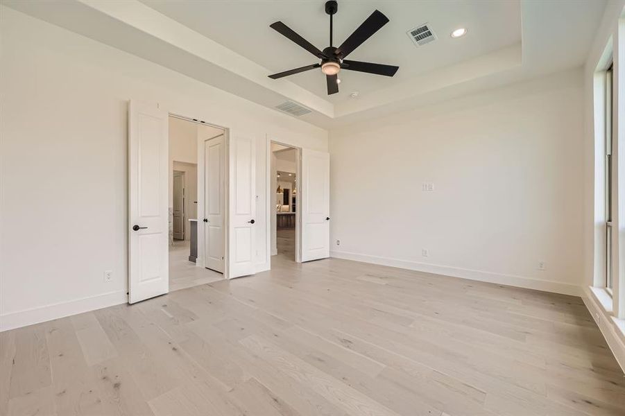 Unfurnished bedroom with a tray ceiling, light wood-type flooring, and ceiling fan