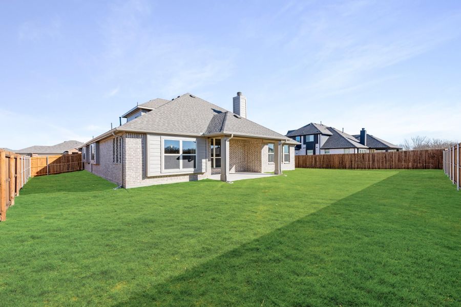 Brick home rear exterior with covered patio, large fenced backyard, and green lawn