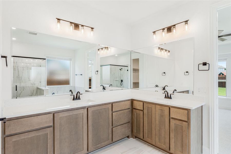 Master bathroom with dual sinks, L-shaped wood vanity, white countertops, and large mirrors above each sink.