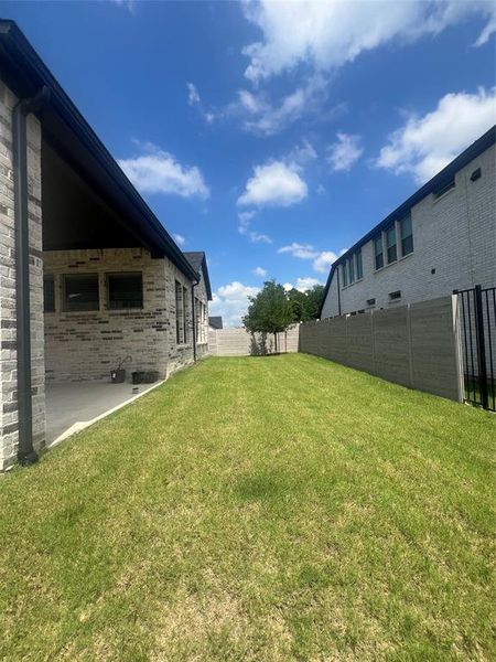 Expansive green lawn with a covered concrete patio, brick exterior, dark gutters, and a privacy fence Expansive green lawn with a covered concrete patio, brick exterior, dark gutters, and a privacy fence