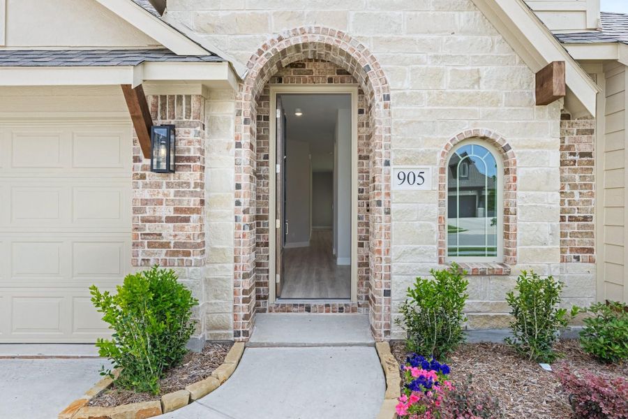 Home entrance with brick and stone arched doorway, house number 905, and landscaped flower beds Home entrance with brick and stone arched doorway, house number 905, and landscaped flower beds