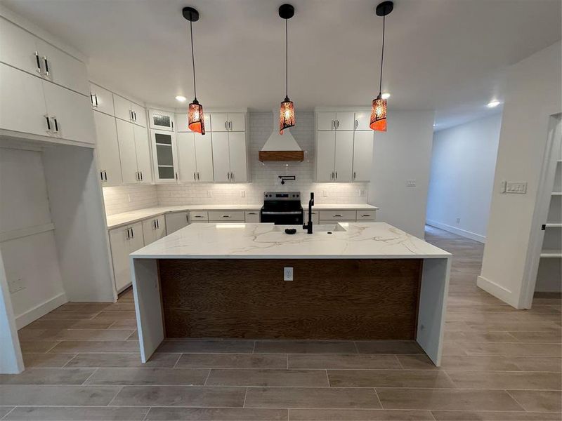 Kitchen featuring light stone countertops, an island with sink, backsplash, white cabinets, and stainless steel range with electric cooktop Kitchen featuring light stone countertops, an island with sink, backsplash, white cabinets, and stainless steel range with electric cooktop