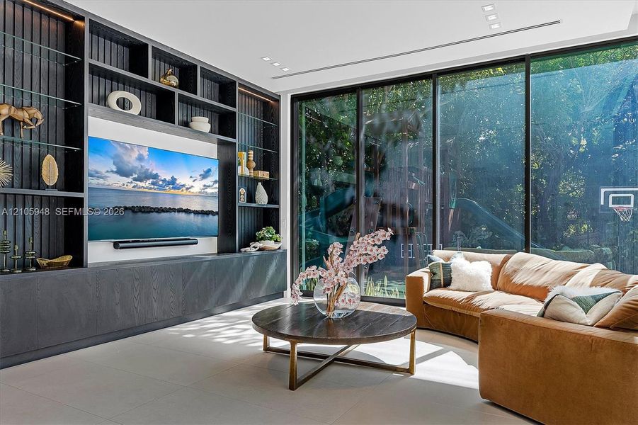 Custom dark-toned, floor-to-ceiling built-in cabinetry featuring integrated shelving, floor-to-ceiling glass walls, large-format tile flooring, and recessed ceiling lighting