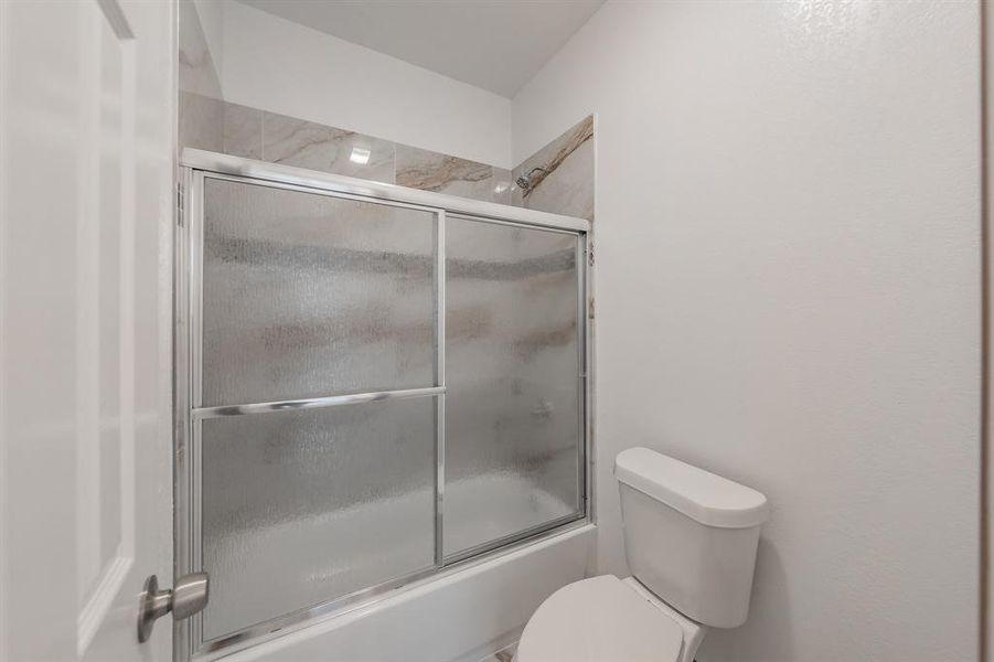 Full bathroom with toilet and bath / shower combo with glass door