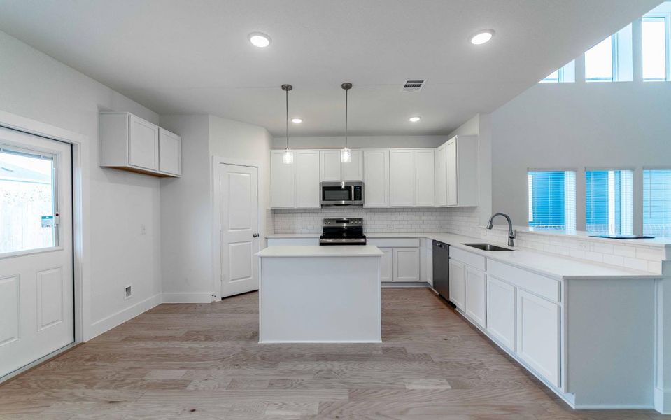 Kitchen with white cabinetry, light wood finished floors, a kitchen island, stainless steel appliances, and decorative light fixtures Kitchen with white cabinetry, light wood finished floors, a kitchen island, stainless steel appliances, and decorative light fixtures