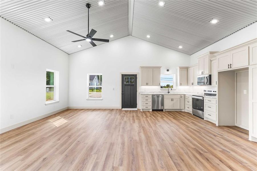 Kitchen with high vaulted ceiling, light countertops, stainless steel appliances, light wood-style floors, and open floor plan Kitchen with high vaulted ceiling, light countertops, stainless steel appliances, light wood-style floors, and open floor plan